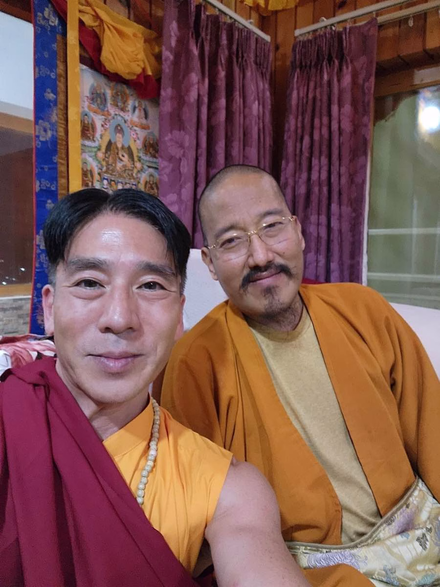 Alex Yamane in maroon and saffron Buddhist robes with a bespectacled lama in a Tibetan shrine room